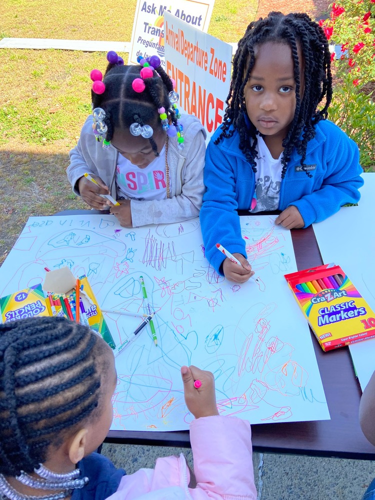 Kids participating in the What Home Means to Me poster contest outside drawing on poster board