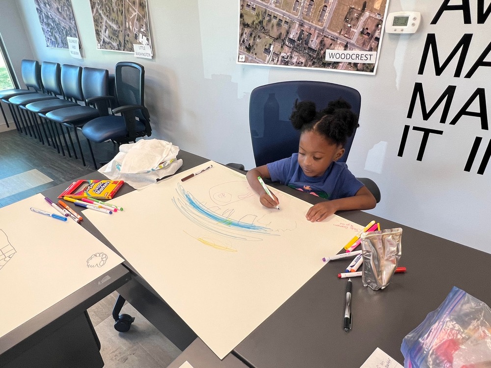 Little girl with afro puffs drawing on poster board inside building