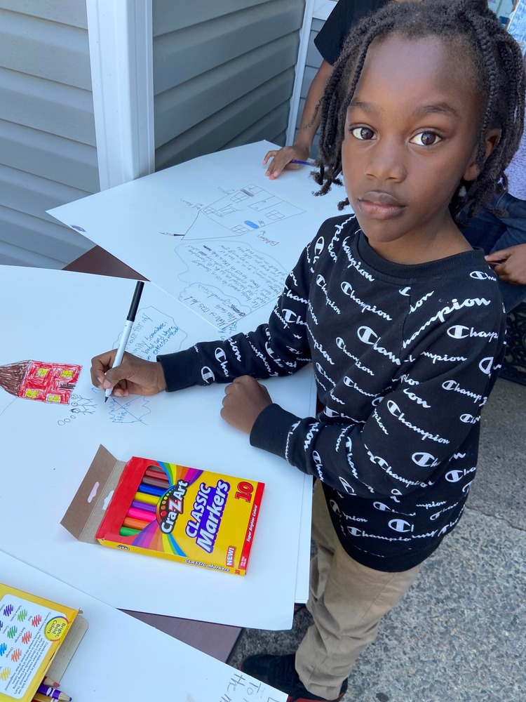 little boy drawing with markers on poster board outside while looking at camera