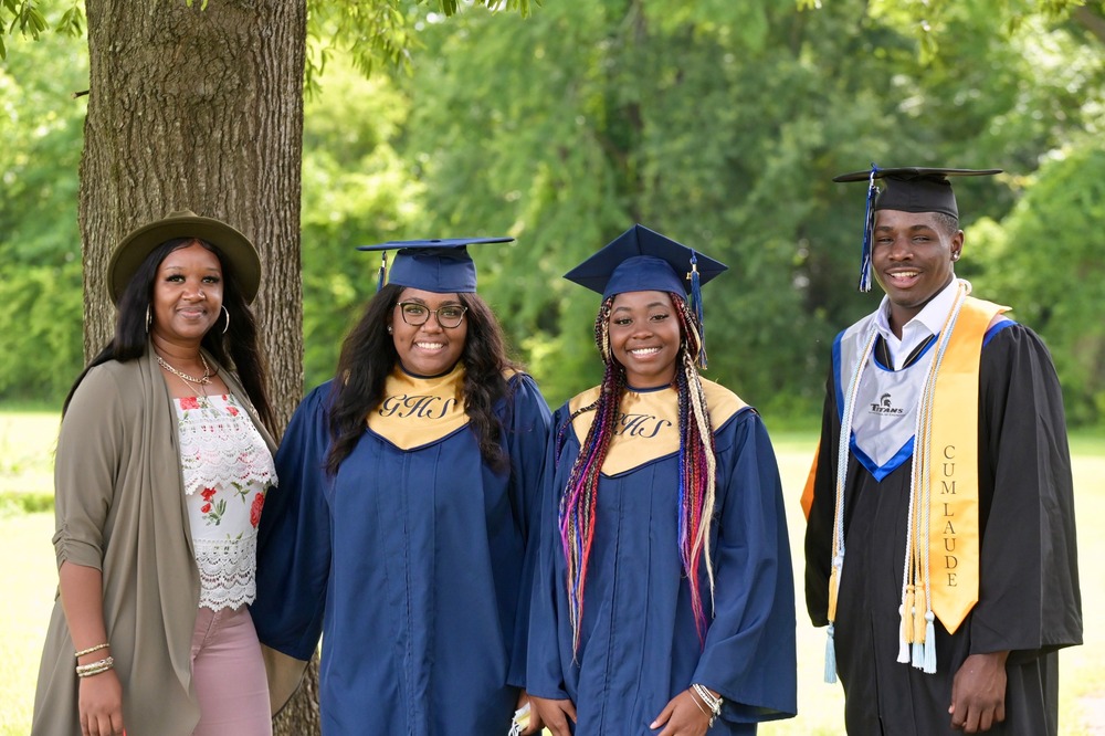 Scholarship reciepients standing outside in their cap and gowns with Resident Services member Deeiah Hayes