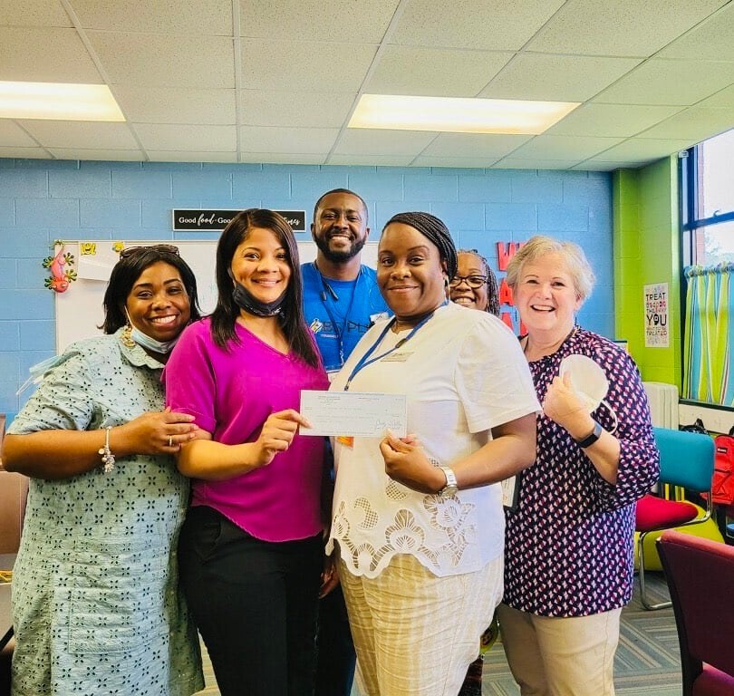 HACG Staff are grouped in a classroom while holding a check to sponsor the Tranquility Garden at Carver Heights.