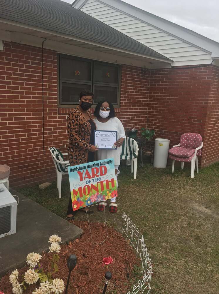 Blanche Davis outside her residence holding a Yard of the Month certificate with HACG Staff member